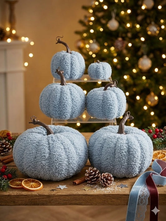 Wholesale set of six light blue sherpa boucle fabric pumpkins in assorted sizes displayed on a wooden table with a warm bokeh Christmas tree background.