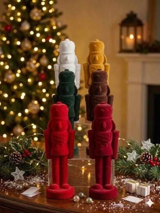 Wholesale bundle of 6 modern minimalist Christmas nutcracker figurines with a matte velvet flocked finish, tiered by color (red, green, brown, white, yellow) in front of a warm festive fireplace.