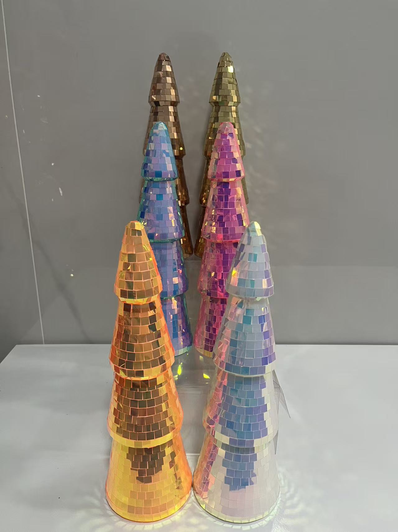 A group of modern disco ball Christmas trees with colorful iridescent mirror tiles in orange, pink, blue, and silver for festive party table centerpiece.